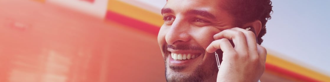 Portrait d'un businessman tunisien souriant en ligne avec son telephone mobile devant une station shell