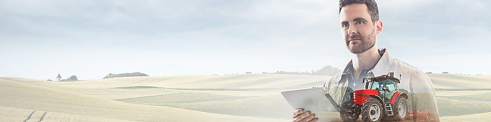 homme lisant un document dans un champ avec un tracteur rouge