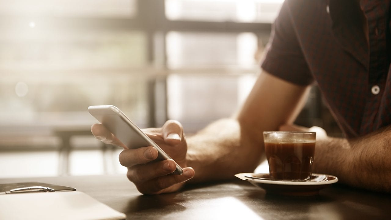 Homme prenant un café tout en consultant son smartphone