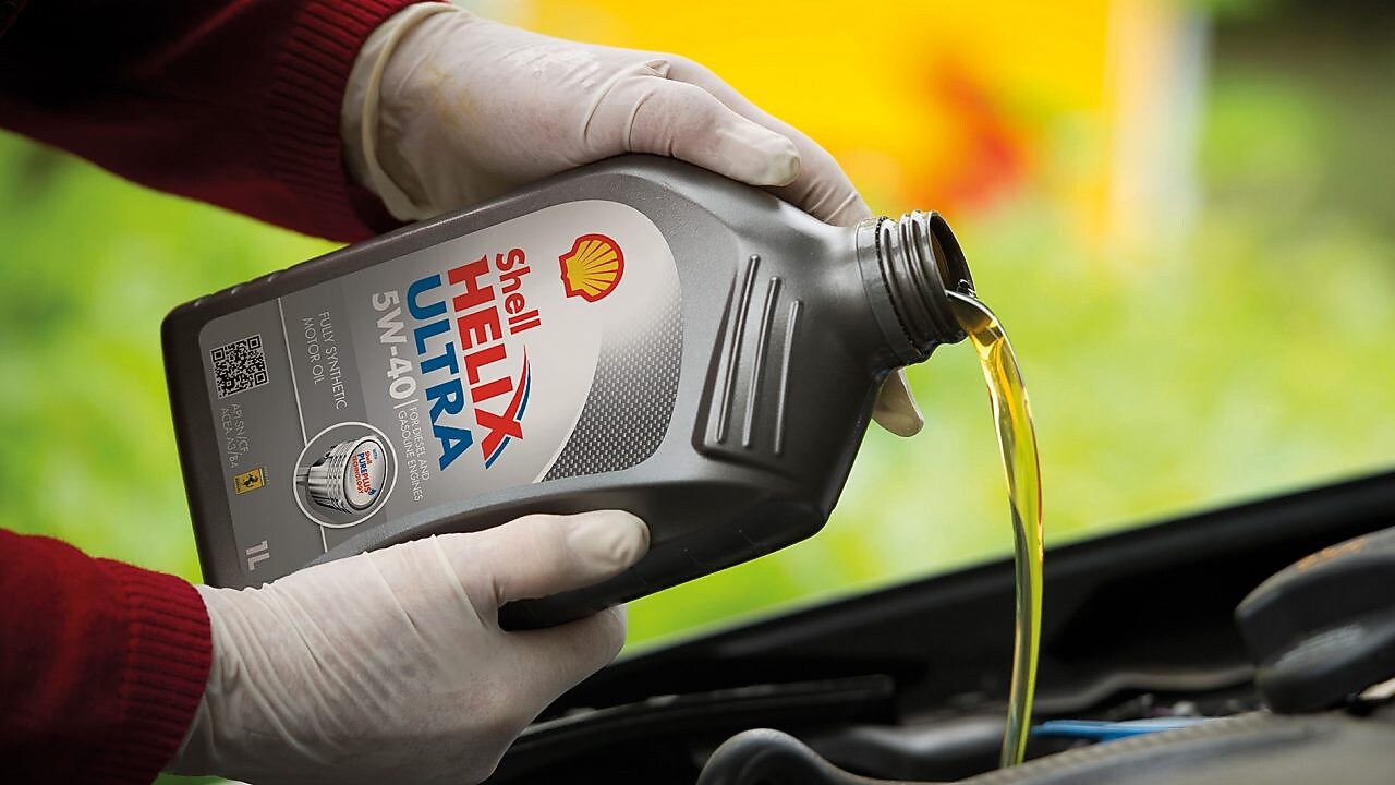 Mécanicien en train de verser de l'huile Shell Helix dans le moteur d'une voiture