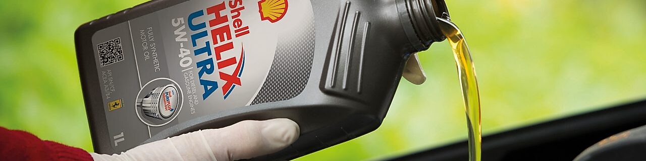 Mécanicien en train de verser de l'huile Shell Helix dans le moteur d'une voiture