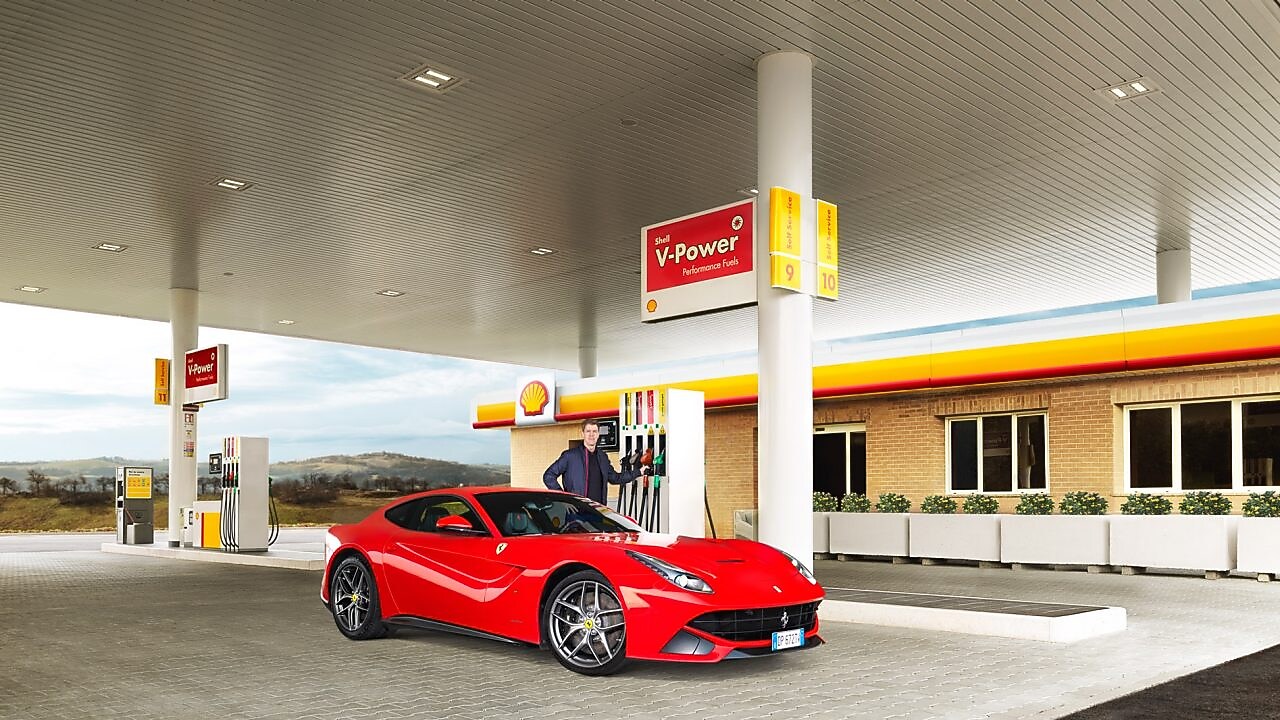 Une Ferrari rouge arrêtée à la pompe d'une station Shell avec un homme qui s'apprête à faire le plein