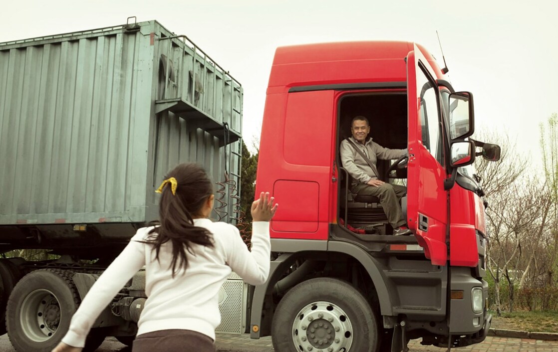 Homme dans une cabine de camion rouge avec porte ouverte saluant sa fille