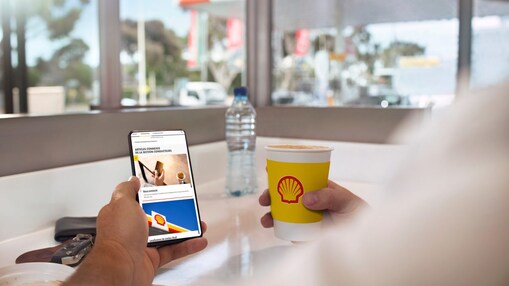 Client en train de consulter l'application mobile Shell en buvant un café dans une station Shell