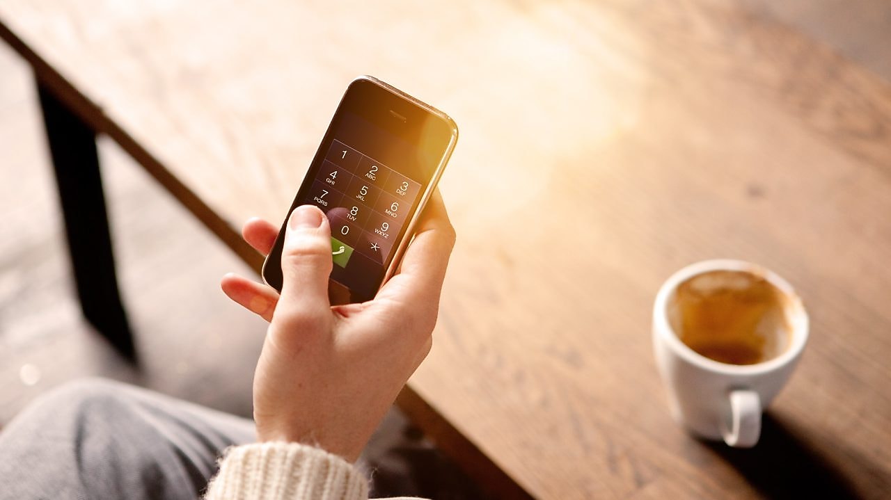 Homme tenant un téléphone portable et buvant un café